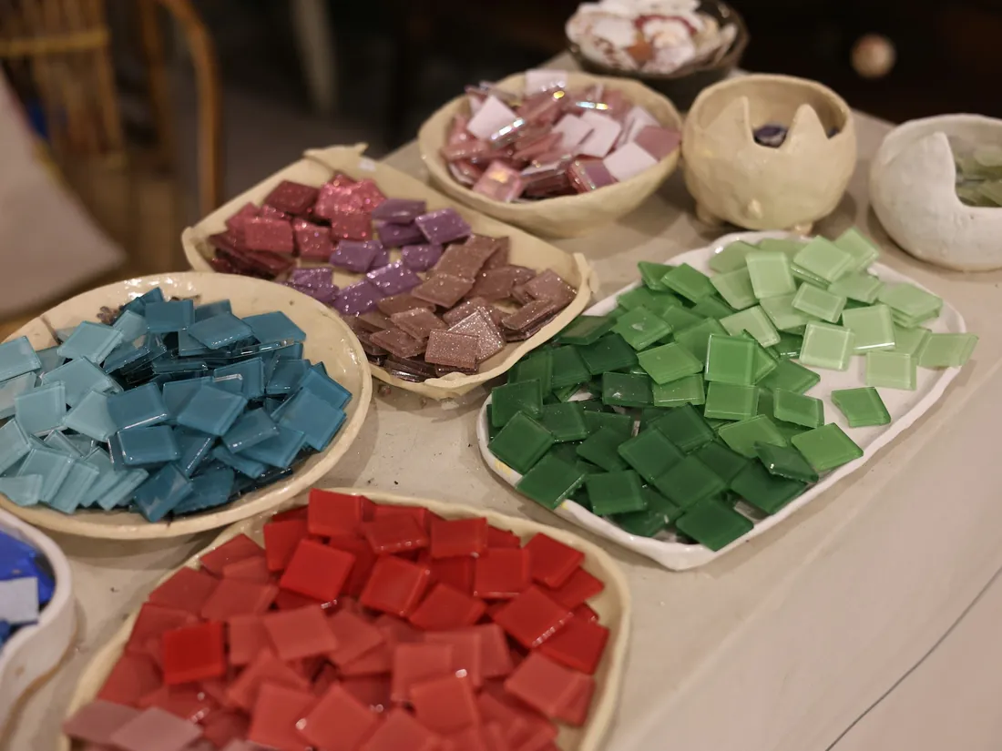 Teselas de vidrio de colores clasificadas en recipientes sobre una mesa de taller de mosaico